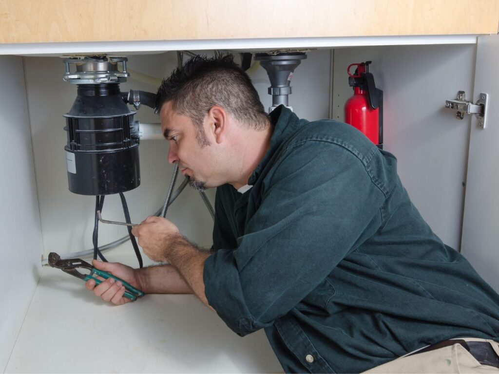 Professional plumber repairing a garbage disposal under a kitchen sink in St. Louis, MO
